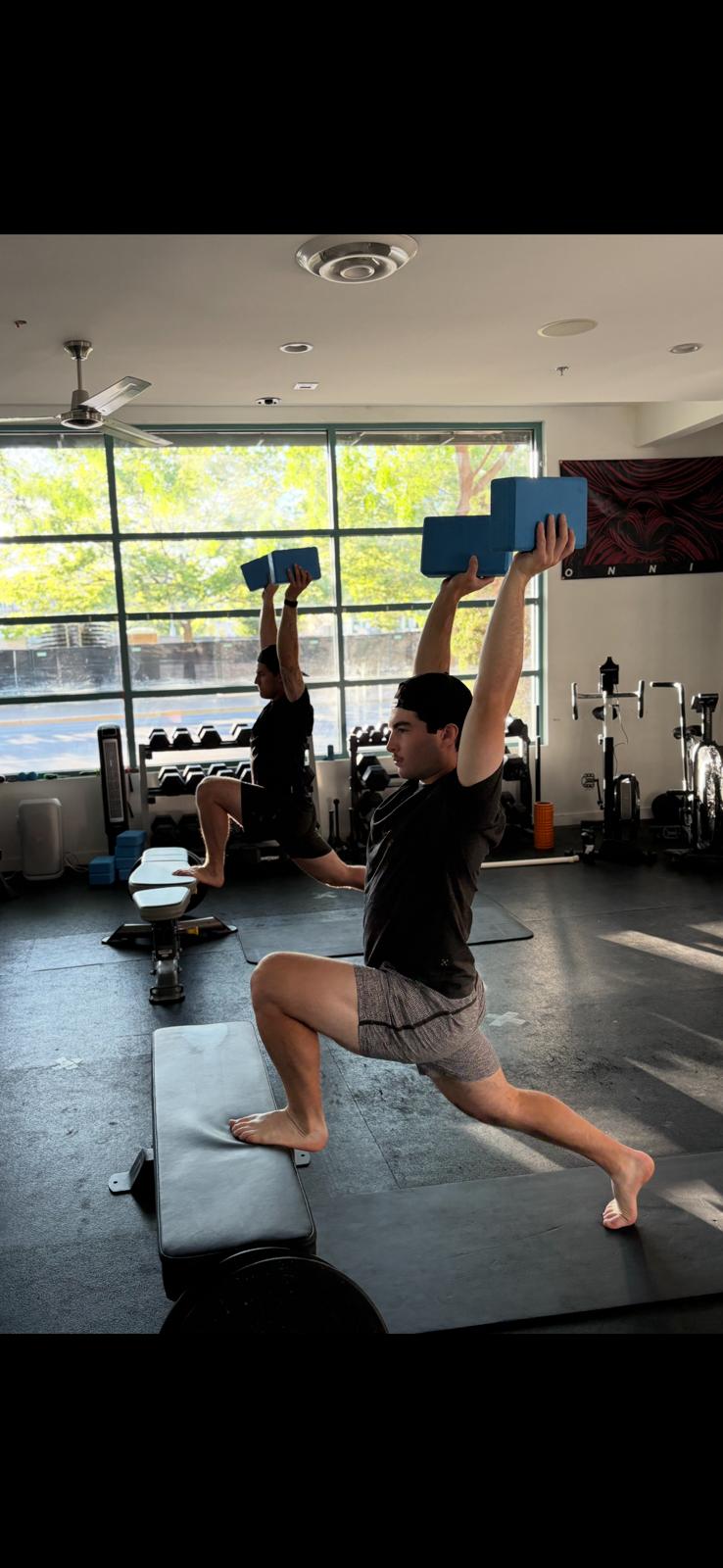 Athletes training kneeling overhead mobility with poles in a gym class